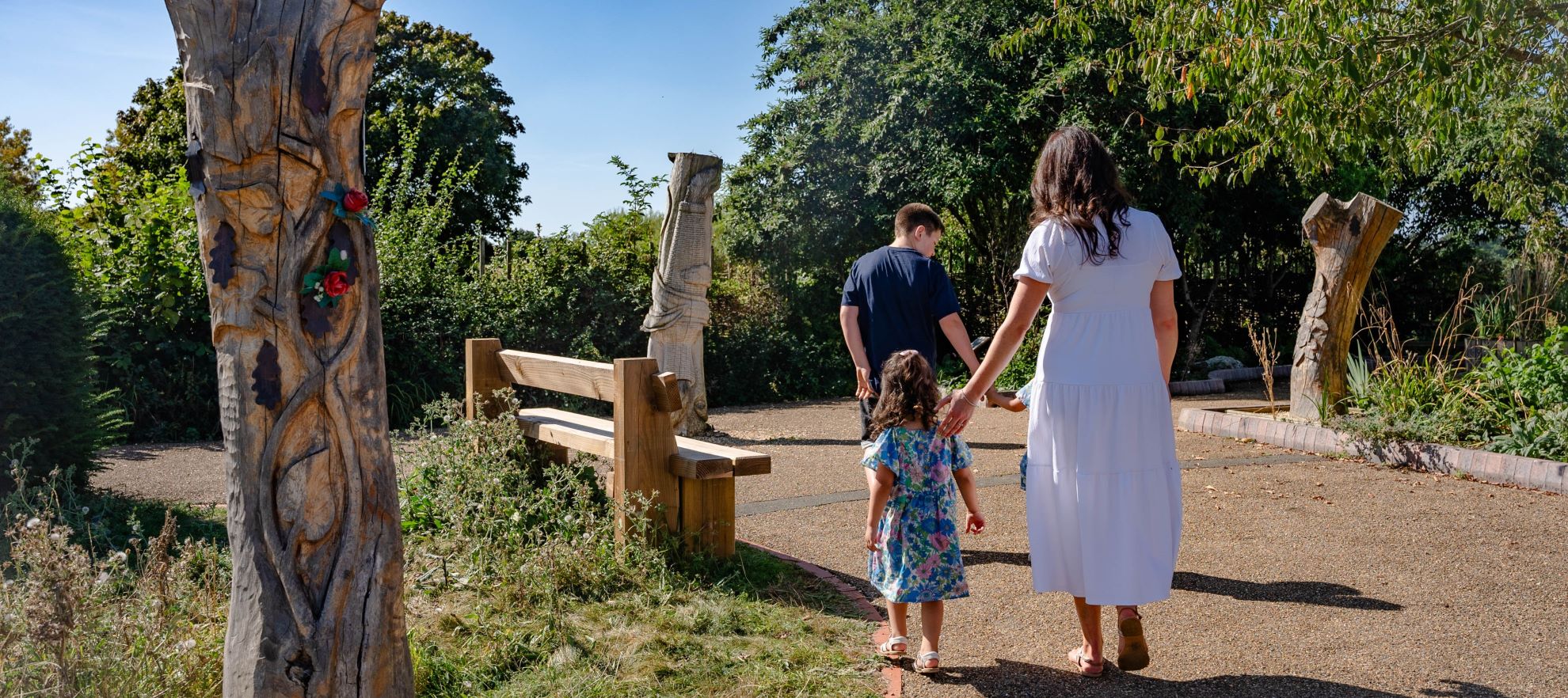 A family walking down a a path next to a wooden sculpture displaying bronze celebration leaves