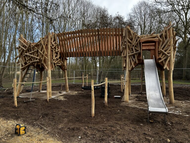 wooden climbing frame with slide set in woodland