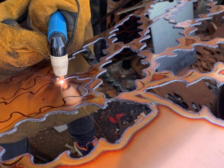 a welder cutting out celebration leaves from a sheet of bronze metal
