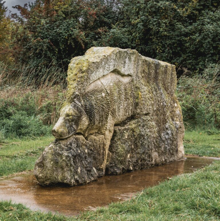 stone sculpture of a wolf in a landscape setting.