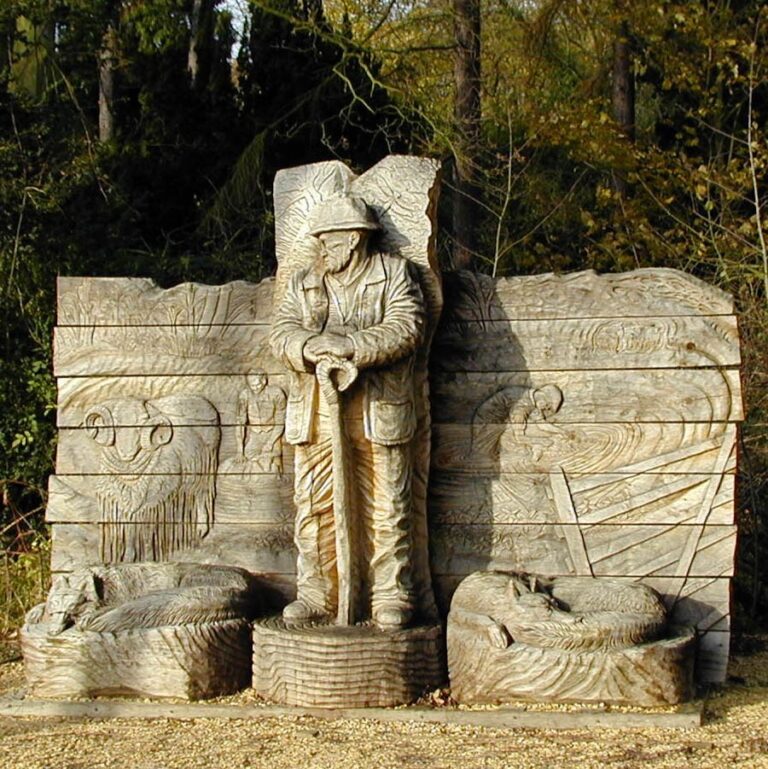 Wooden sculpture showing a shepherd and sheep, set in woodland.