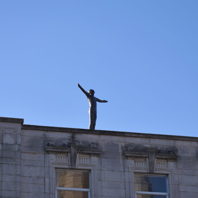 Sculpture of a figure on top of a city centre building.
