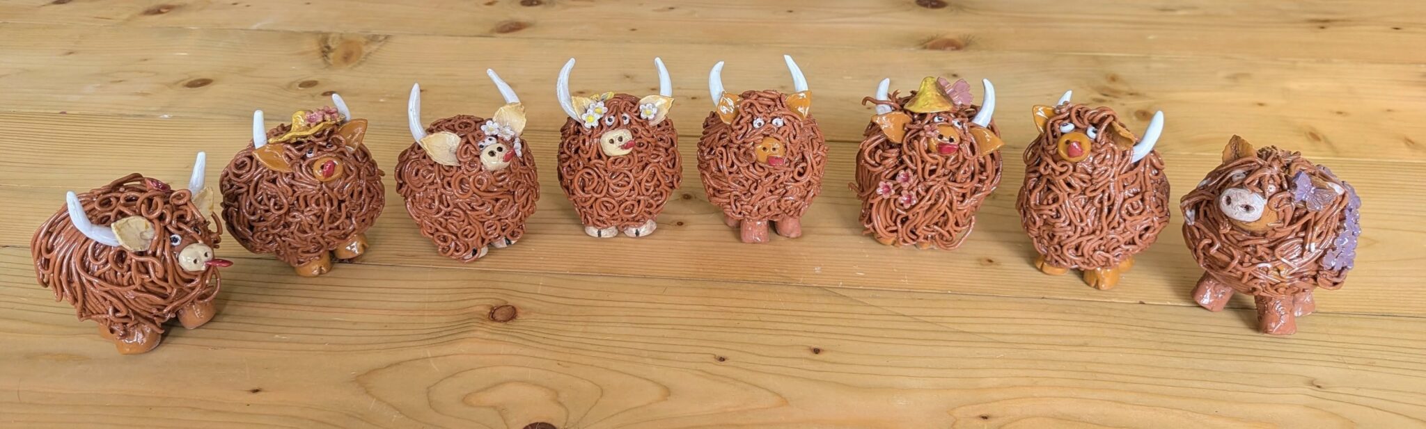 pottery highland cows lined up on a wooden desk