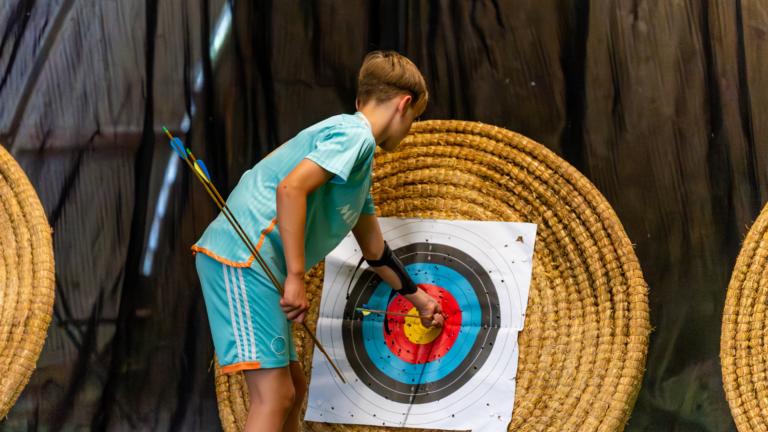 Boy taking archery arrows out of a archery target