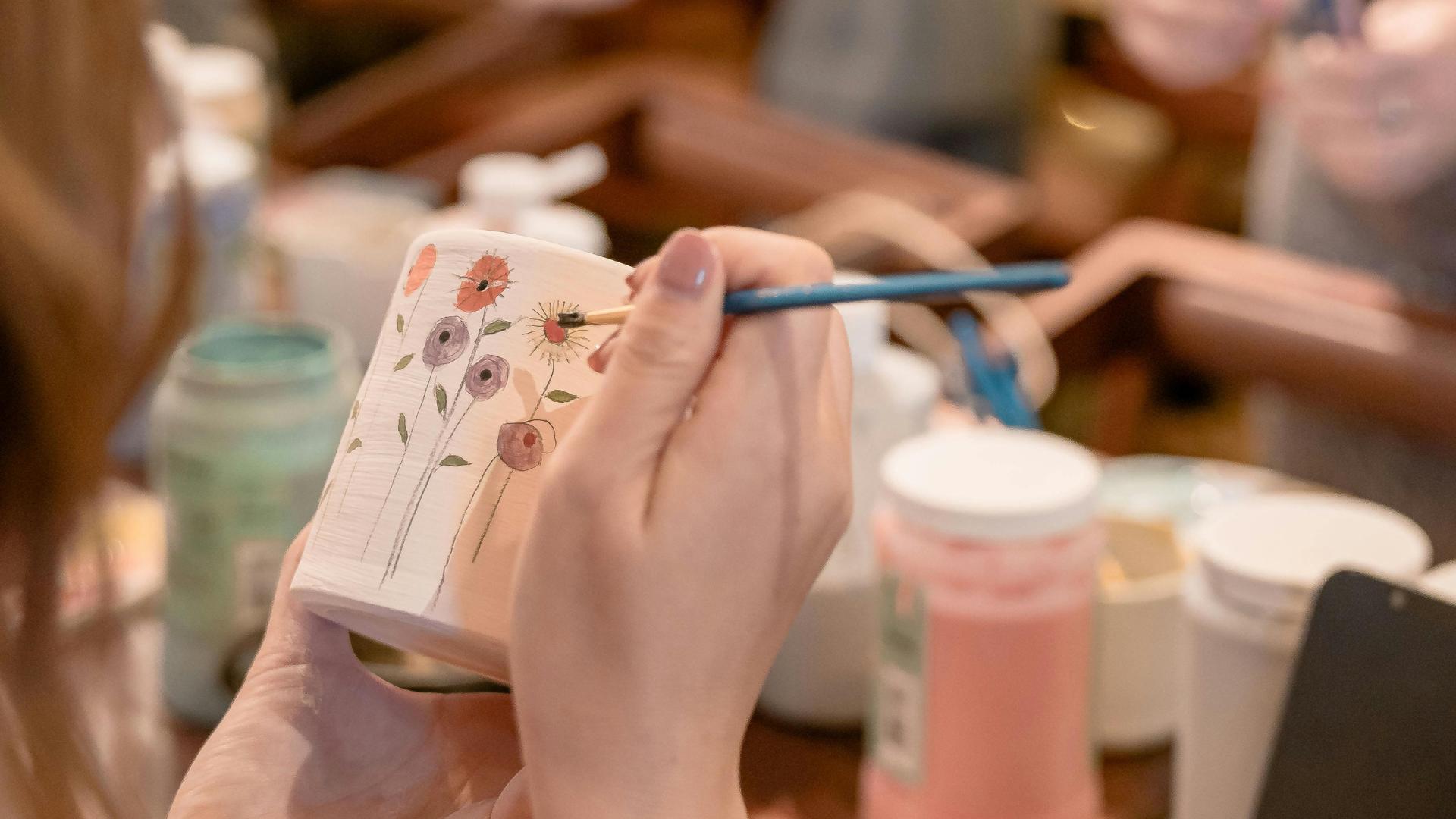 Female painting a ceramic mug with a floral design