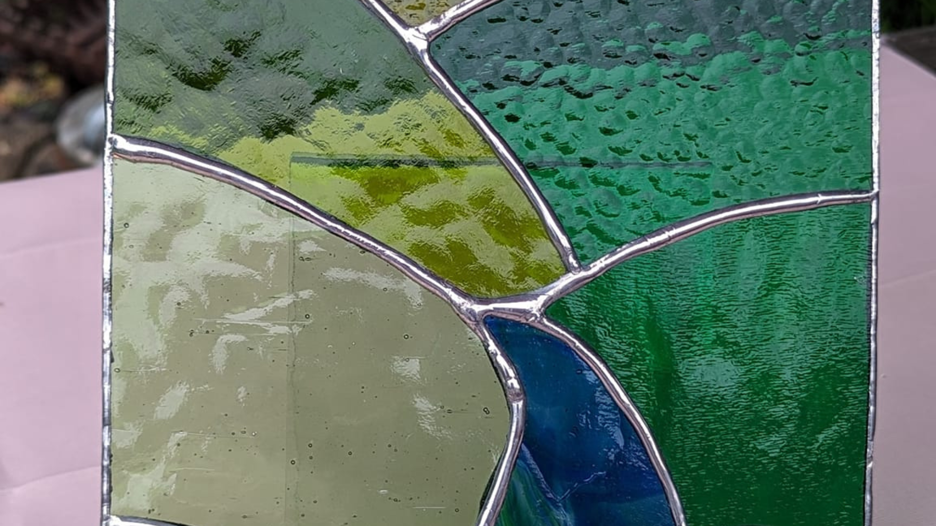 A piece of stained glass art in greens and blues