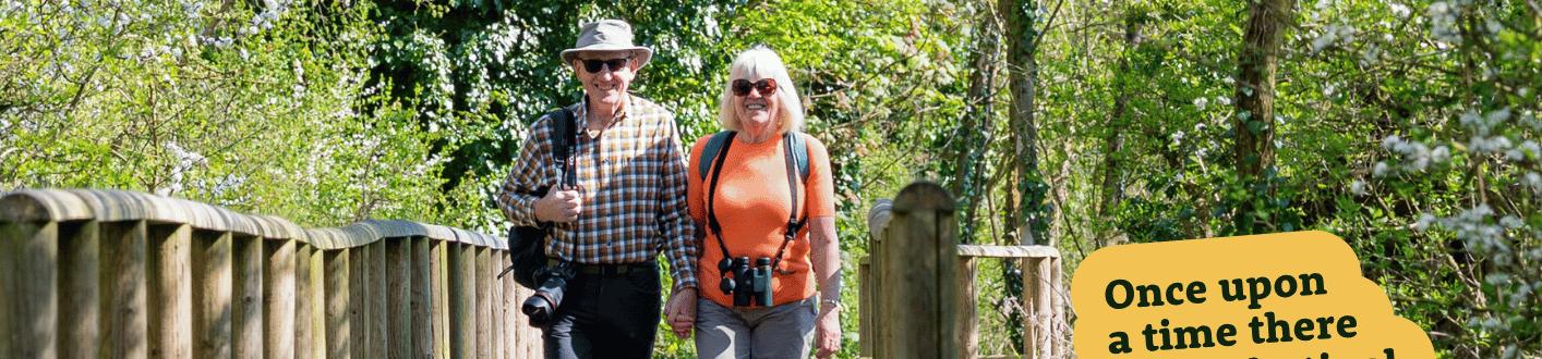 Elderly couple walking on a wooden boardwalk through a spring woodlands.