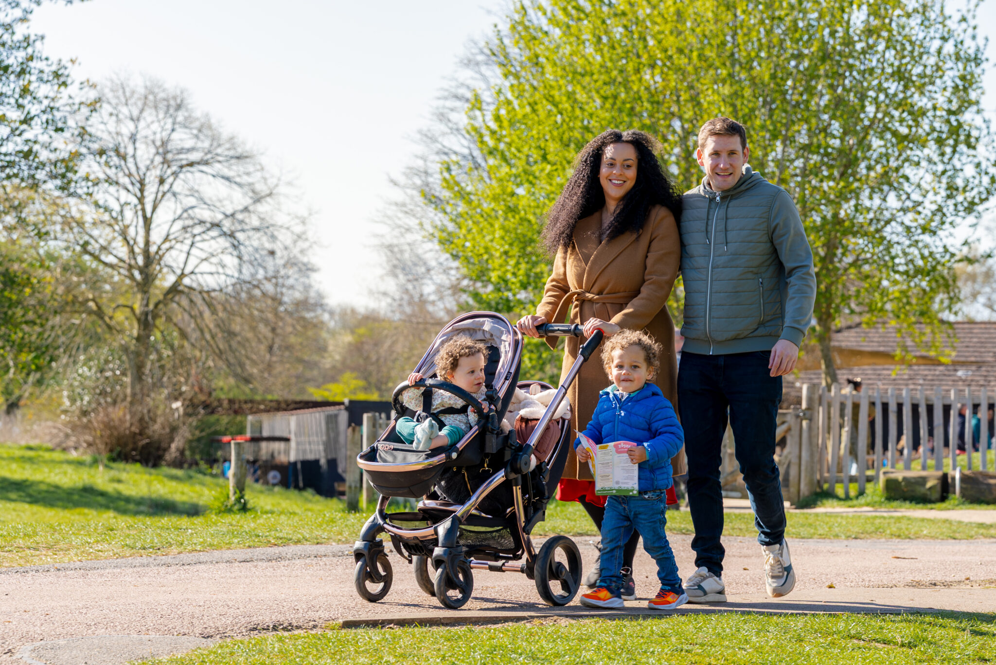 Young family with toddler in a buggy and small child walking round Ferry Meadows