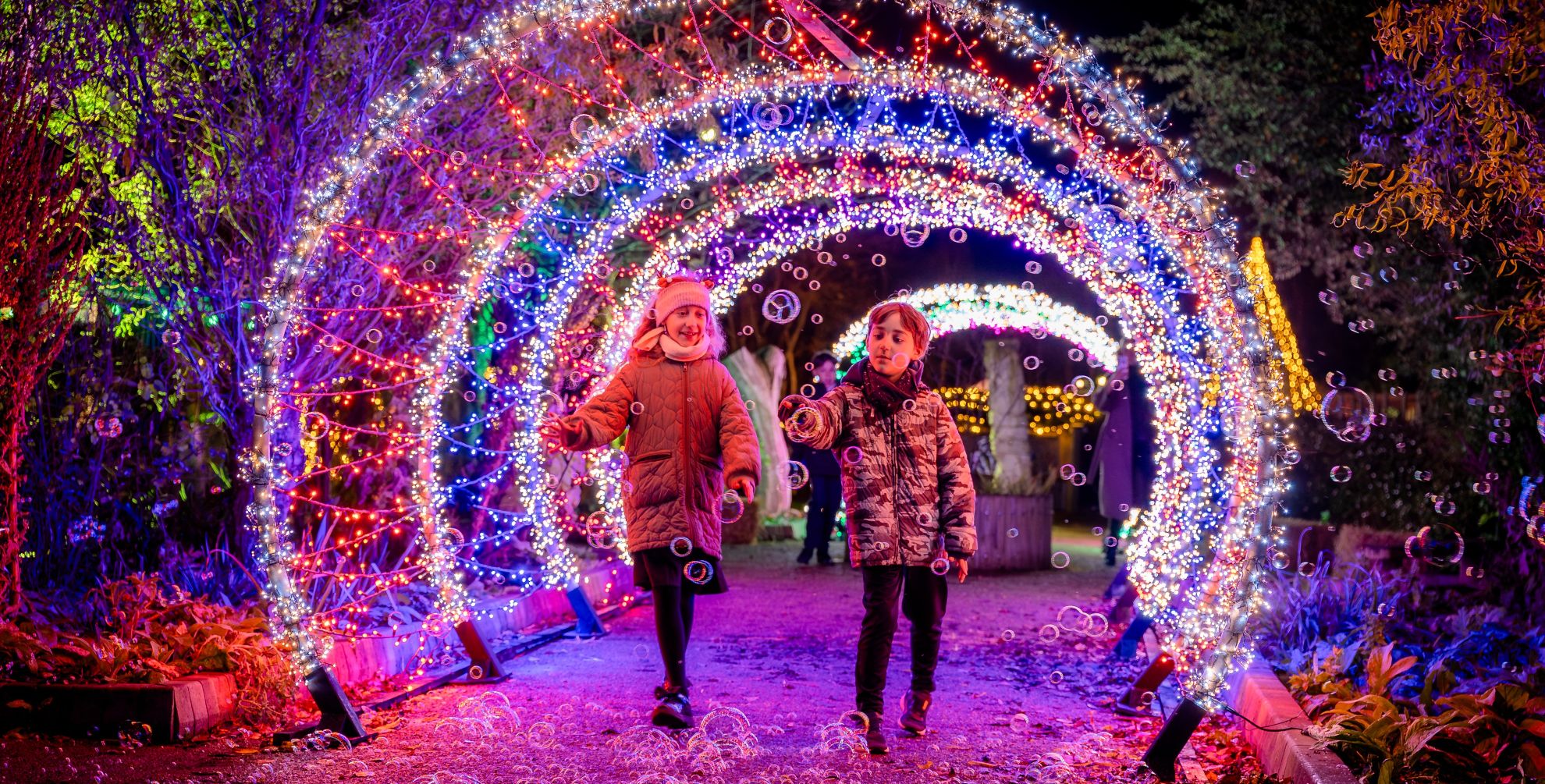 Girl and boy walking under a festive light tunnel lit in different colours at a Christmas event