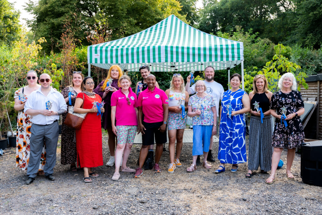 Group of people holding awards, standing in a garden with a gazebo behind.