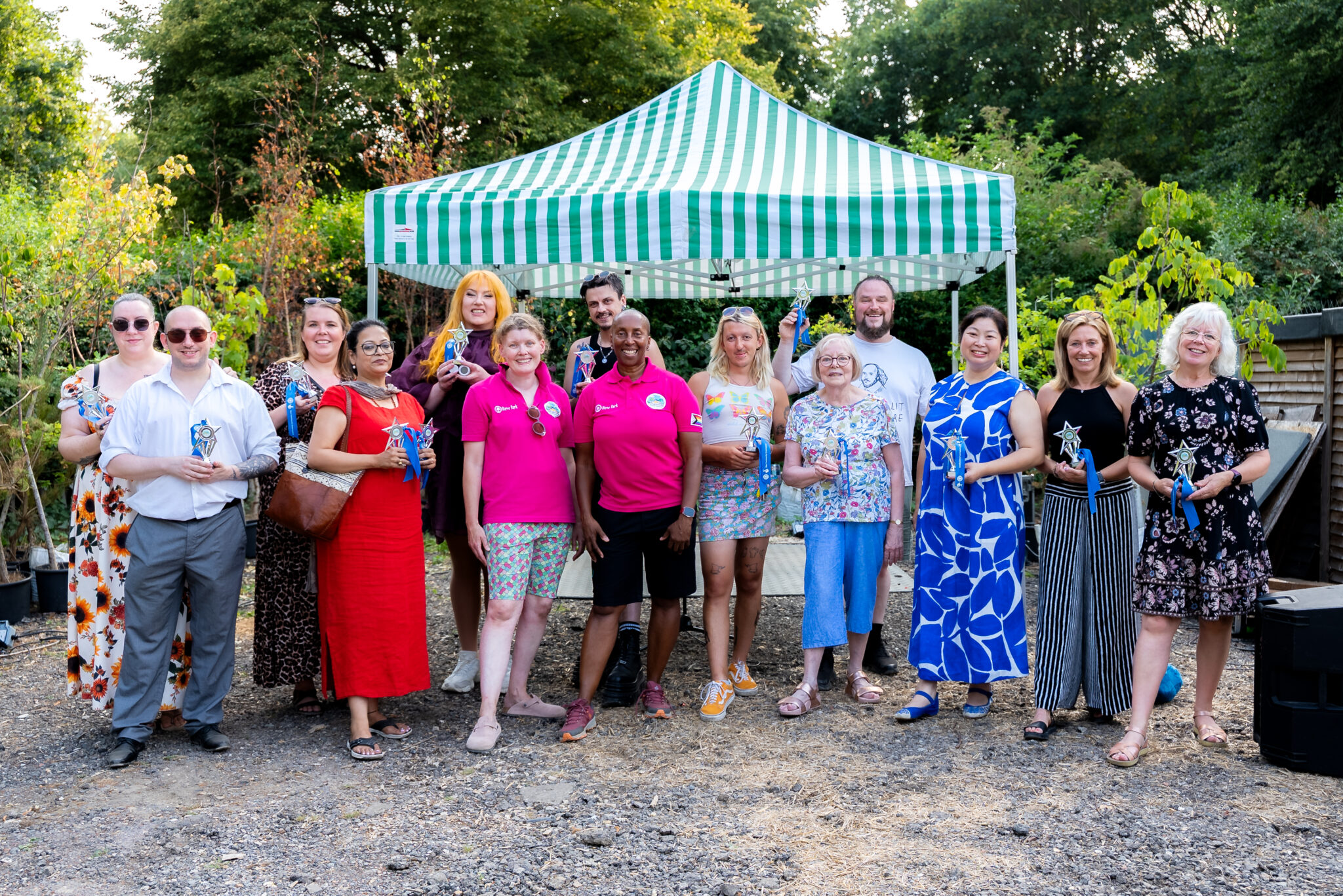 Group of people holding awards, standing in a garden with a gazebo behind.