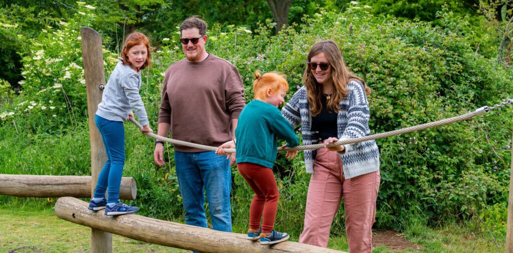 Young family climbing on a wooden pole at a country play park