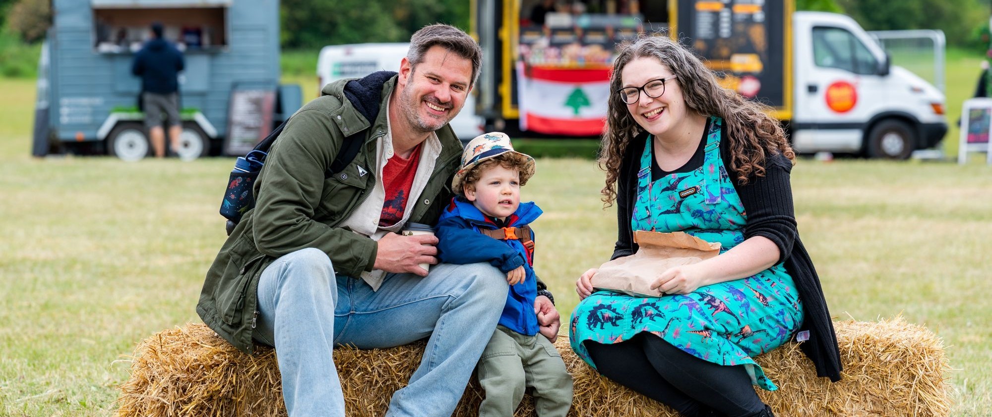 Mum, dad and young boy at an outdoor festival sat on haybales
