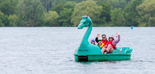 Young family waving from a green dragon pedalo on a lake