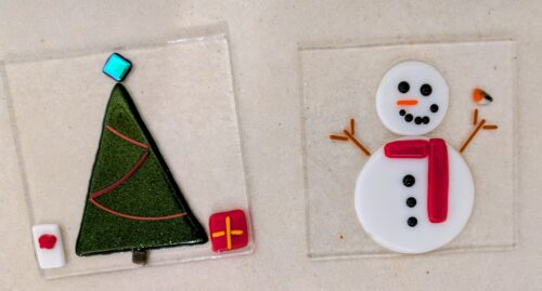 two glass coasters, one featuring a christmas tree and one featuring a snowman